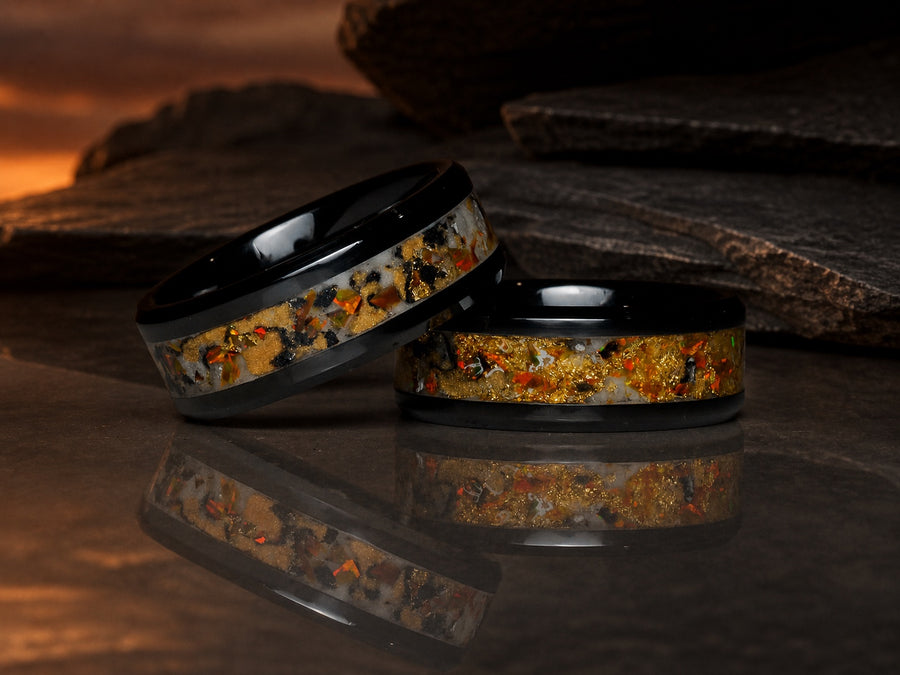Two Gilded Eventide rings resting on reflective volcanic stone at eventide