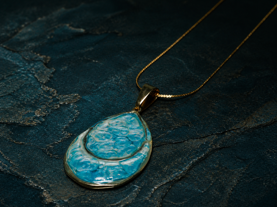 Deep Time Atelier double teardrop pendant on a dark mineral surface