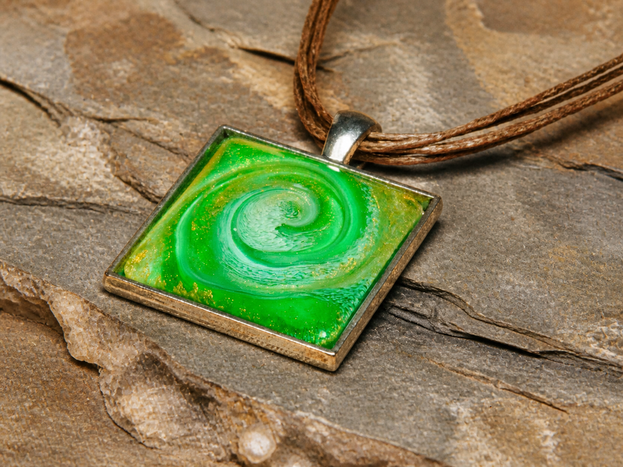 Close-up silver square pendant with vivid green resin spiral and brown leather cord