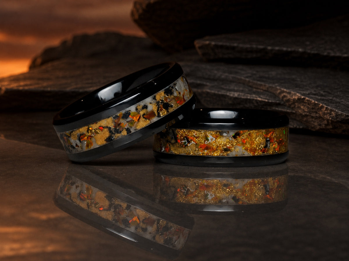 Two Gilded Eventide rings resting on reflective volcanic stone at eventide