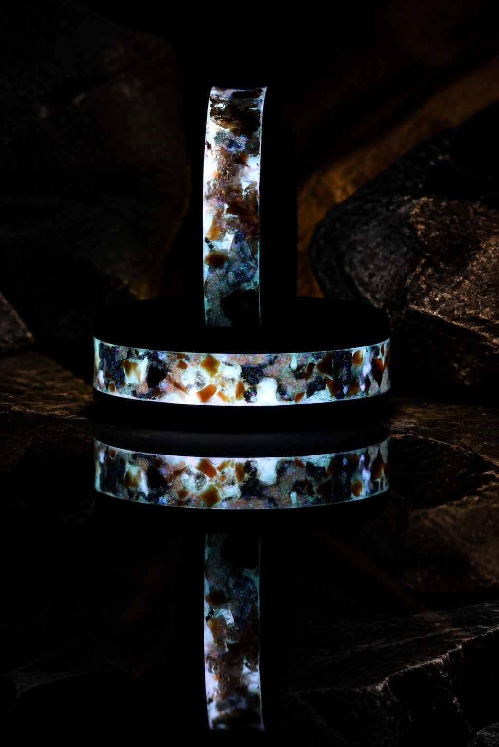 Long-exposure glow detail of Gilded Eventide rings in a dark mineral setting
