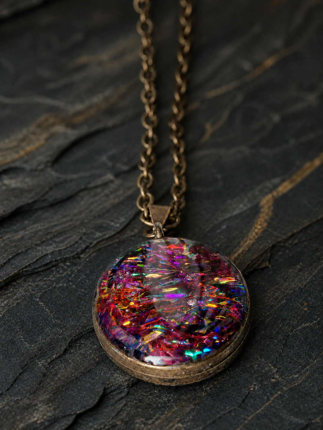 Aurora Fire oval pendant and antique brass chain on dark geological slate