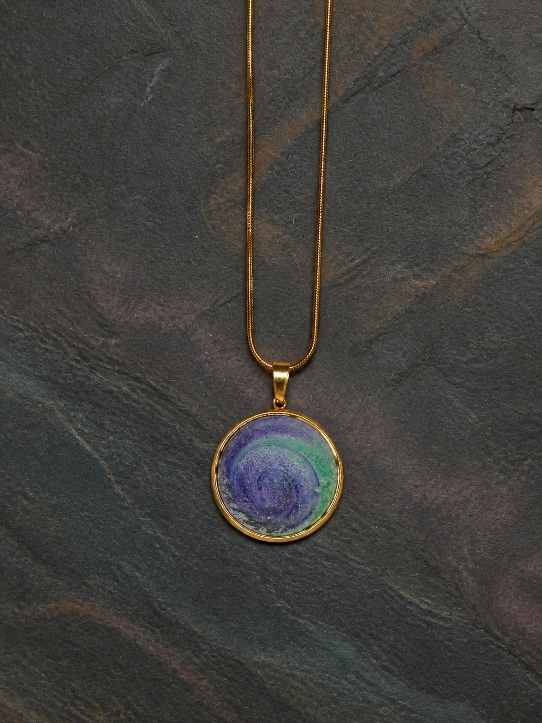 Aurora Well 18K gold-plated round pendant with gold snake chain on dark mineral slate