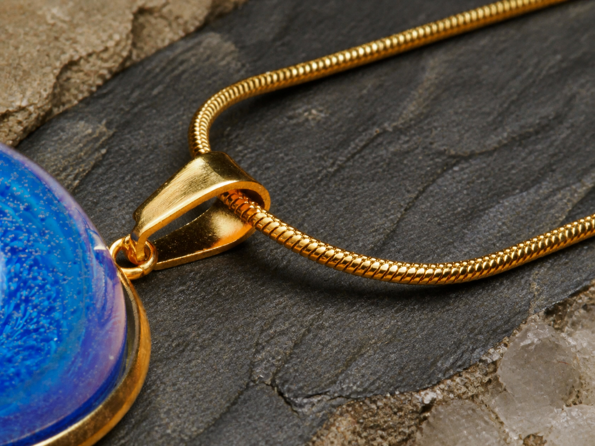 Gold-plated bail and chain attached to blue circular resin pendant over slate