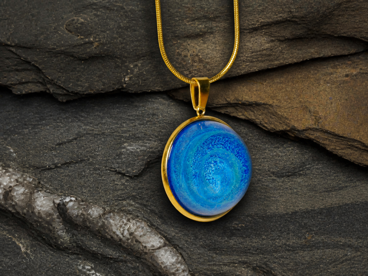 Blue round resin pendant with gold-plated chain on dark stone surface