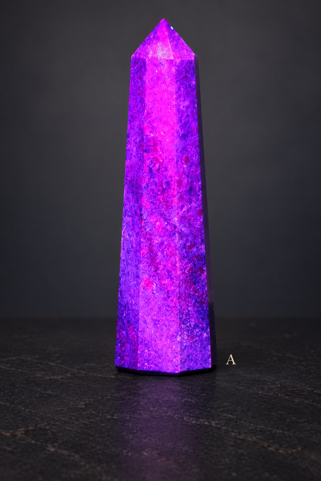 A UV-lit ruby in kyanite obelisk labelled A against a dark graphite gallery background