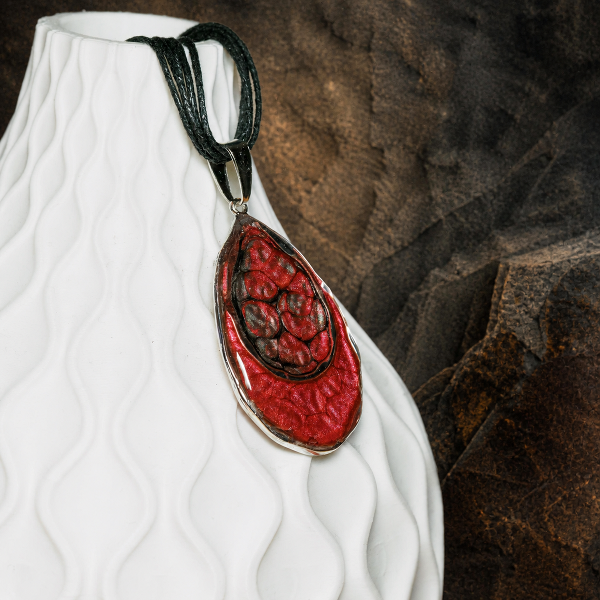 Ember Tide Double Teardrop Necklace close-up on a sculptural white display form with dark mineral stone background