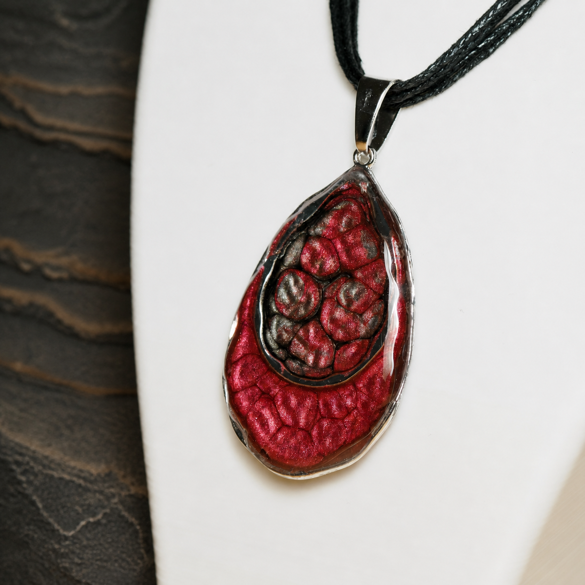 Close-up of the red enamel and resin Ember Tide double-teardrop pendant on a black necklace