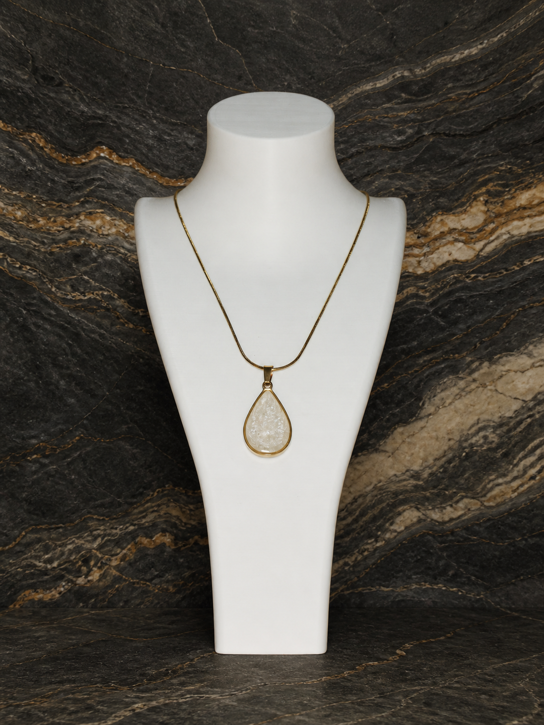 Teardrop pendant and gold-plated snake chain displayed on a necklace bust against mineral strata
