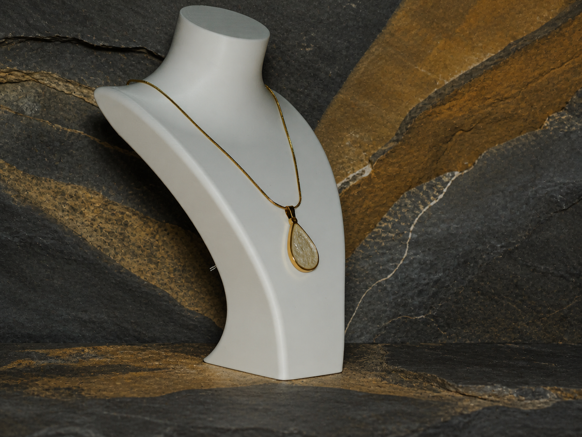 Angled view of teardrop pendant and gold-plated snake chain on a necklace bust with rock texture