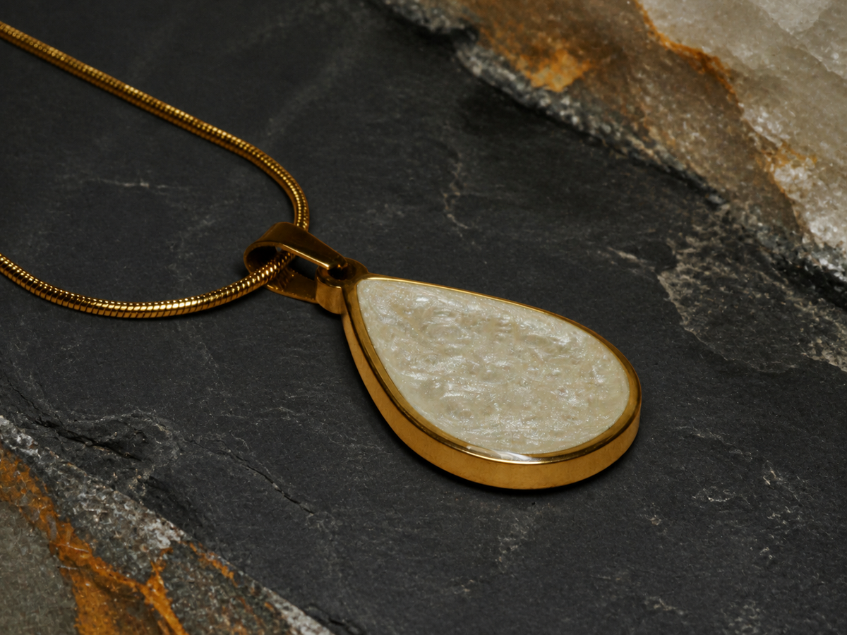 Low-angle teardrop pendant and snake chain on slate with quartz and mineral texture