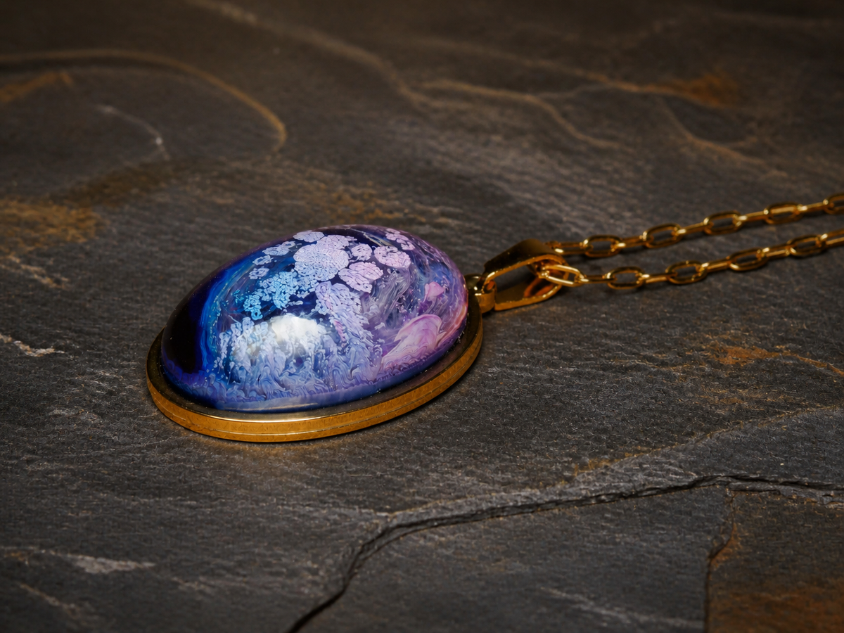 Lavender Reef blue and lavender alcohol-ink resin oval pendant with gold chain on dark stone
