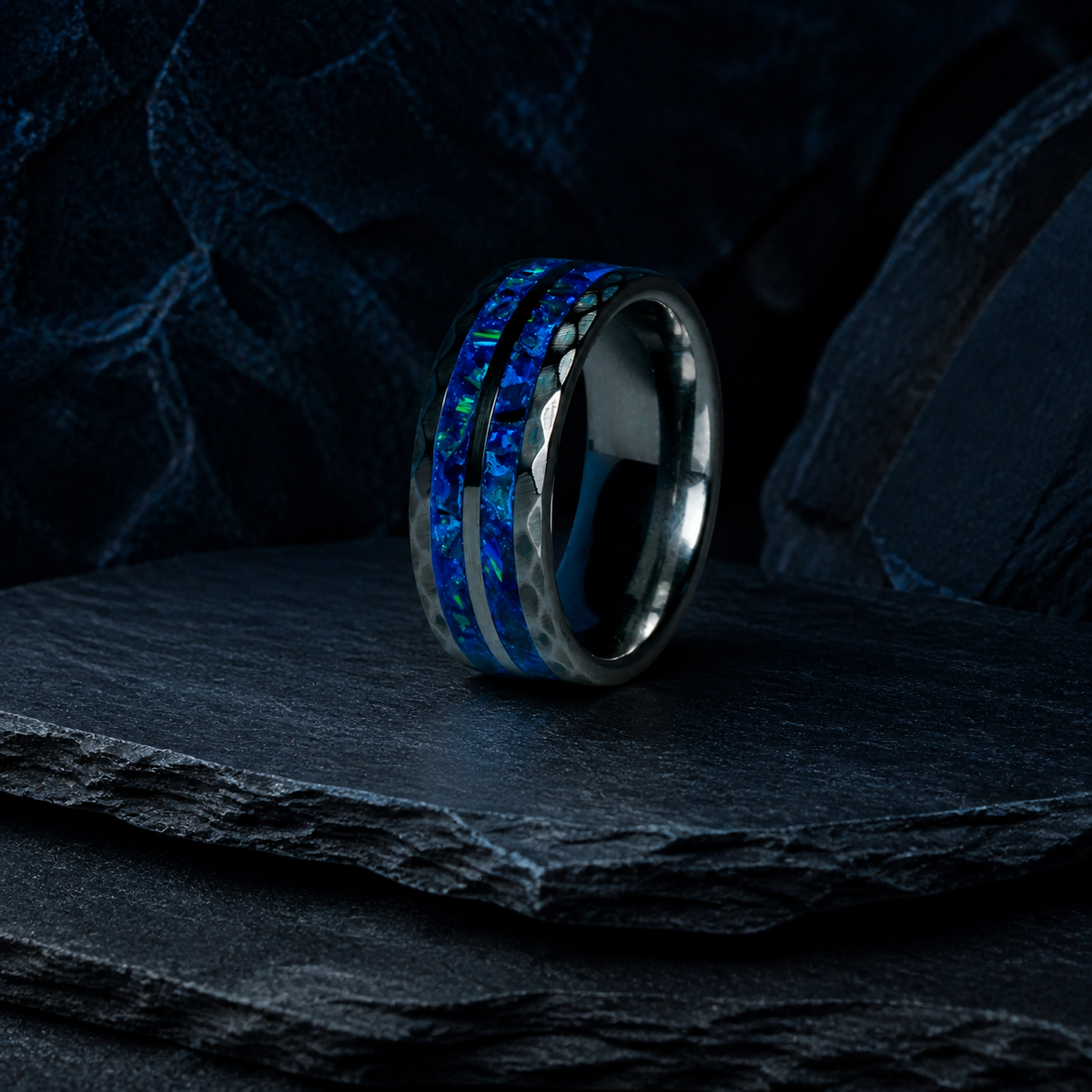 Three-quarter view of Neptune’s Anvil hammered tungsten ring on dark stratified mineral stone