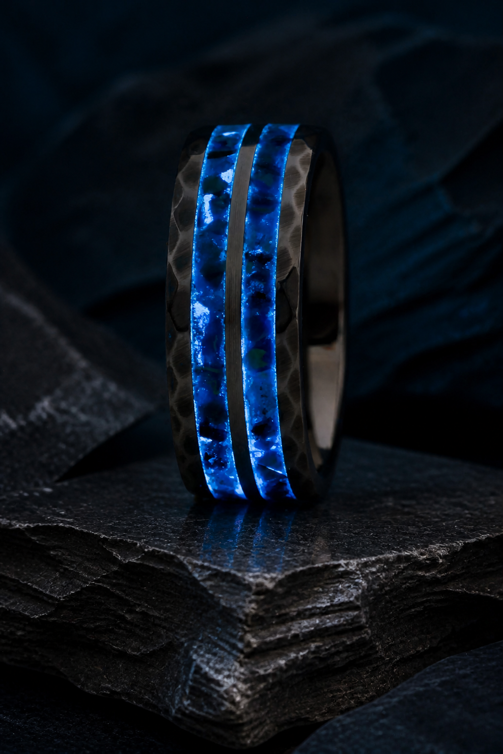 Luminous blue inlay detail of the Neptune’s Anvil tungsten ring on layered charcoal slate