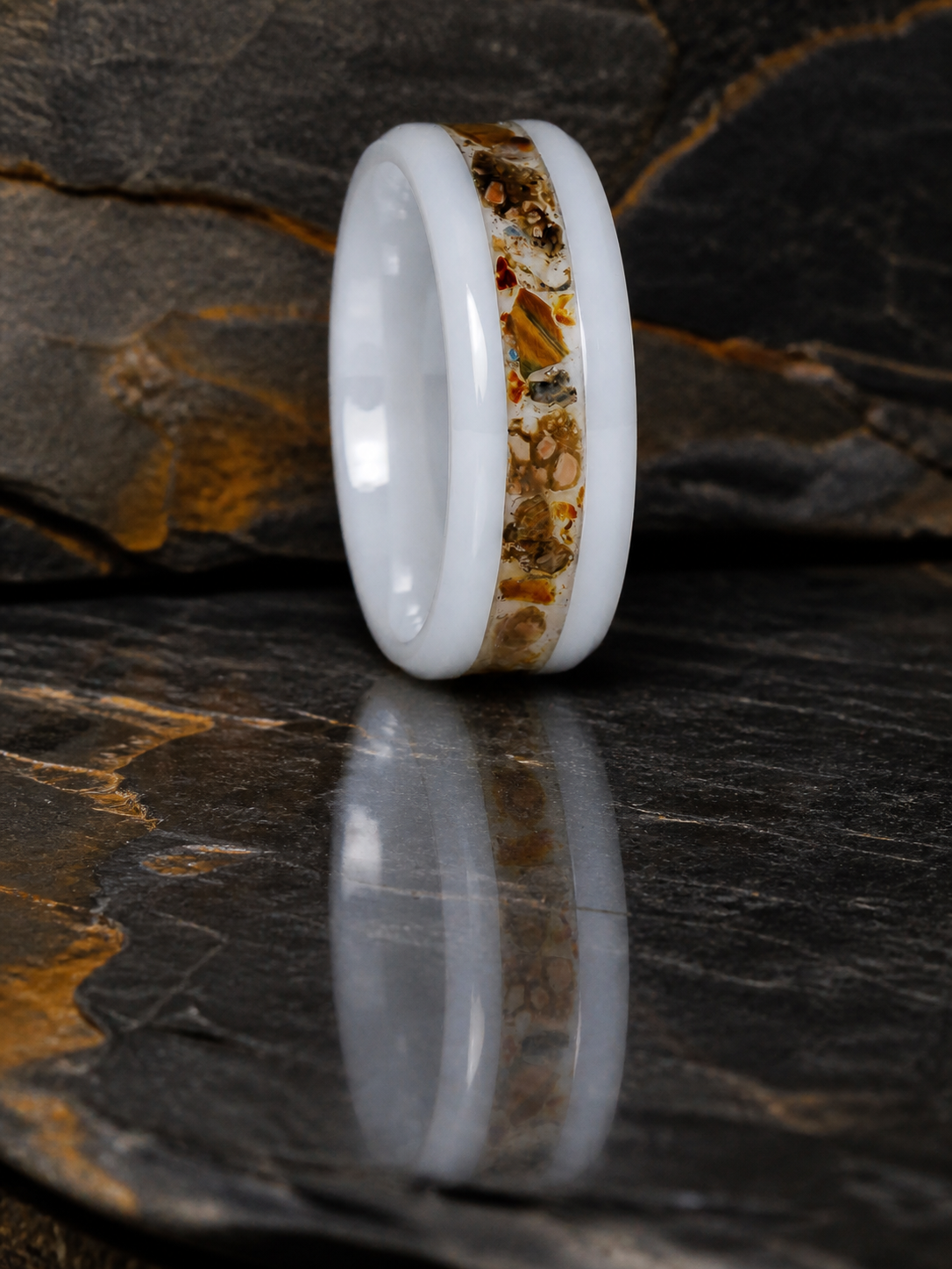 Paleogenesis white ceramic fossil inlay ring standing on reflective dark geological slate