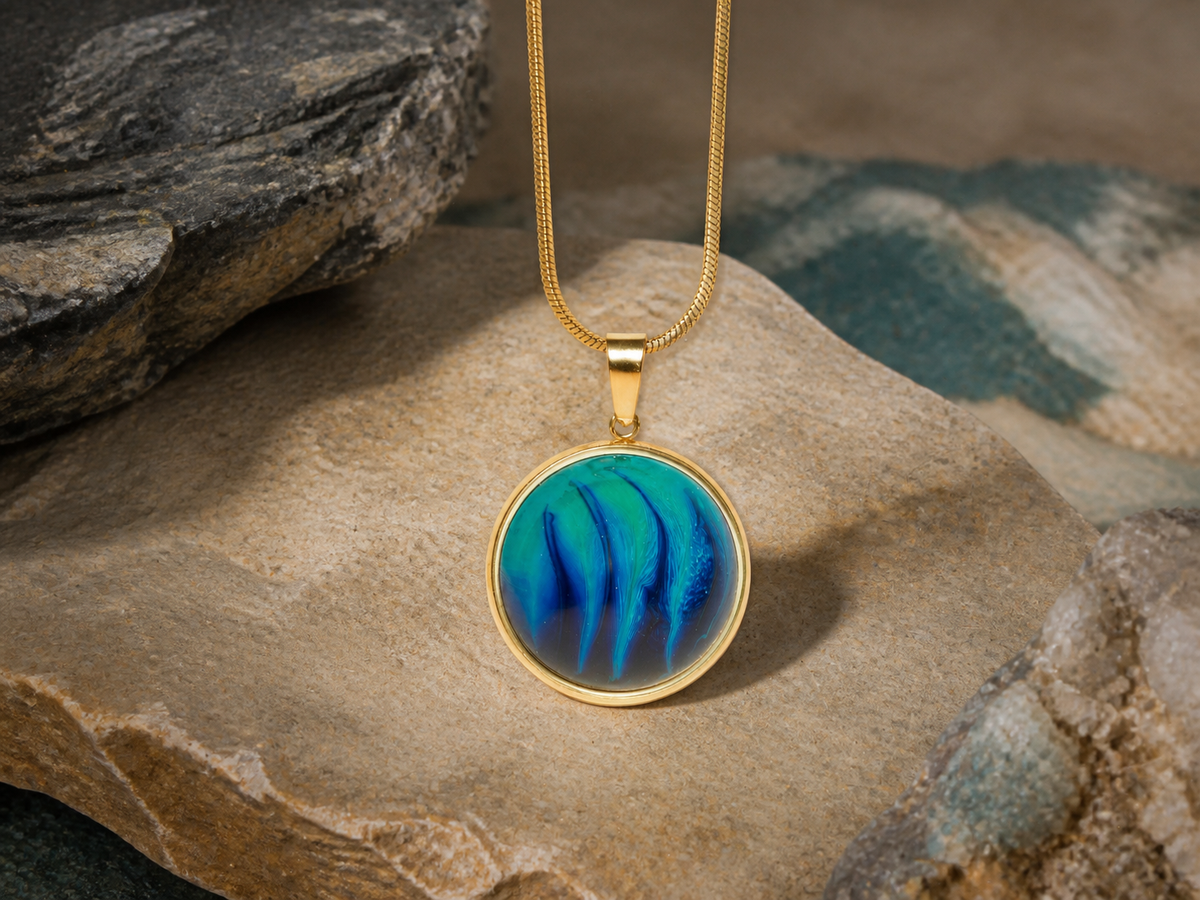 18K gold plated round pendant with blue resin and ink art, close-up on sandstone