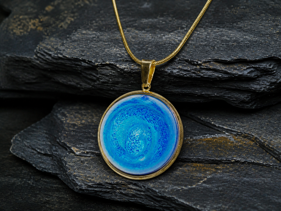 Tethys Gyre cobalt-blue round pendant with gold-plated snake chain on layered charcoal shale