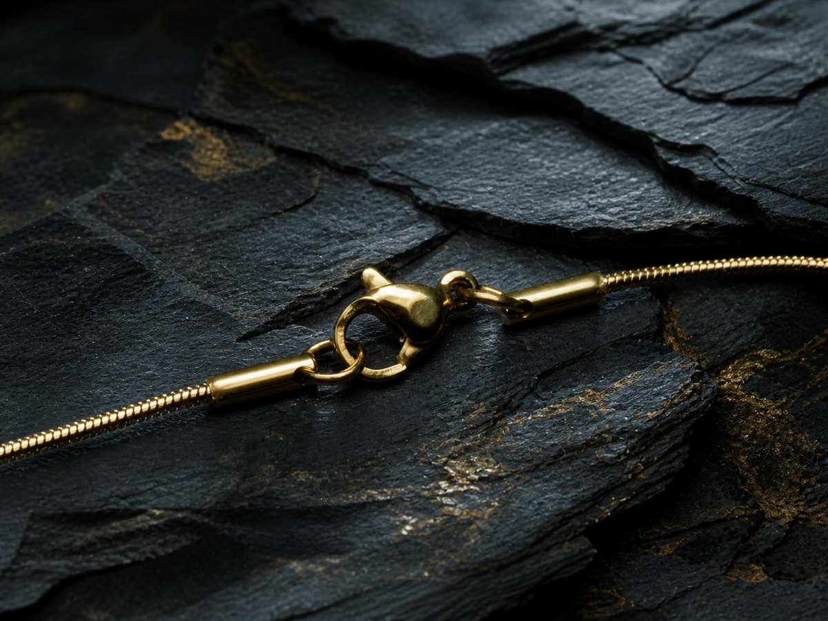 Close-up of the 18K gold-plated stainless steel snake chain and lobster clasp on dark geological stone