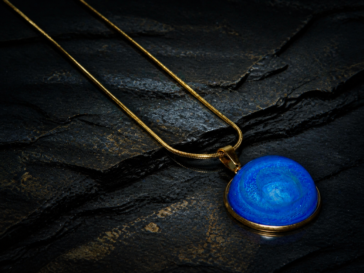 Tethys Gyre blue round pendant with its snake chain arranged across dark mineral strata
