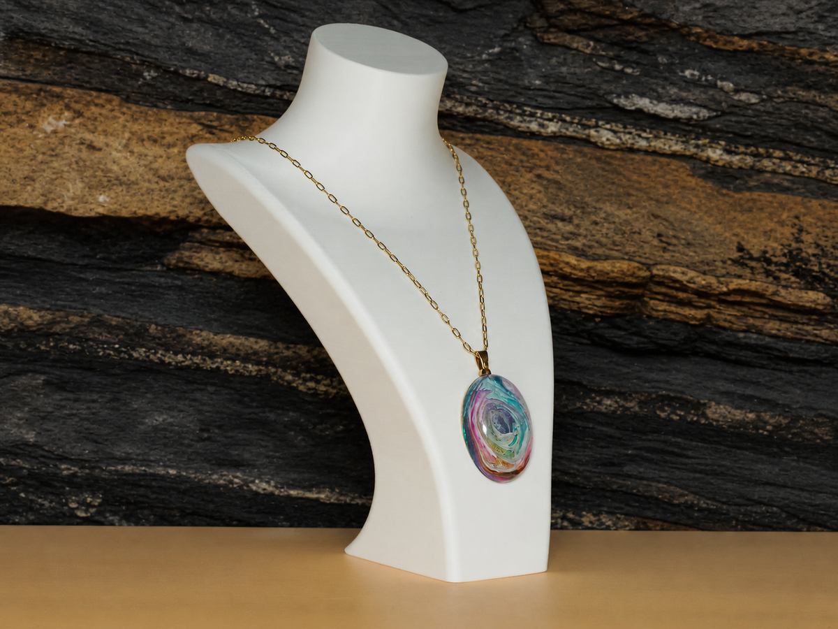Oval pendant and gold-plated chain displayed on an angled necklace bust against stratified rock