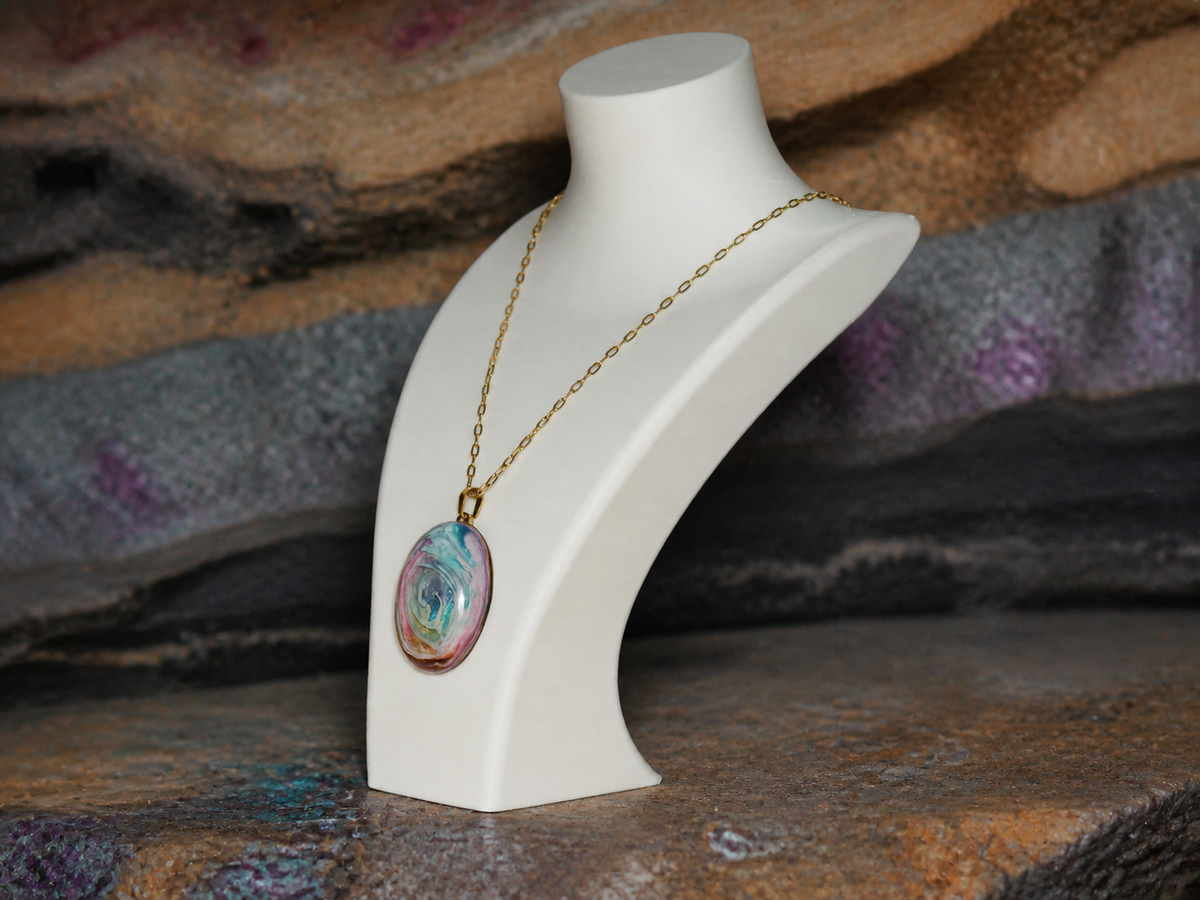 Oval pendant and gold-plated chain displayed on a necklace bust against layered mineral strata