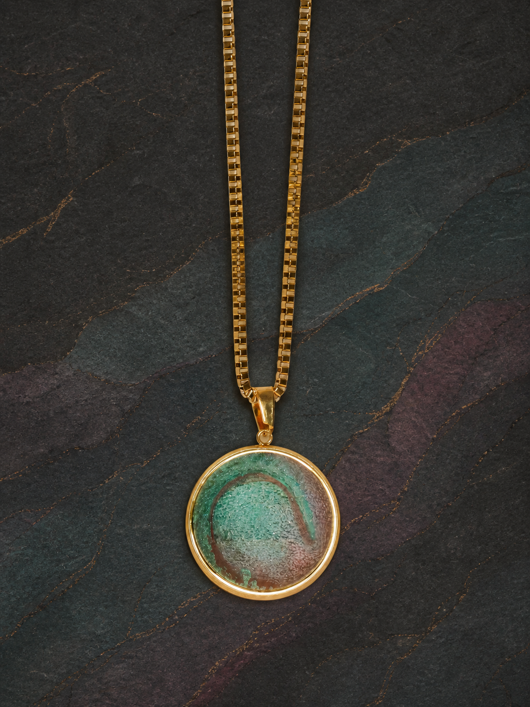 Full view of the Tidal Patina round pendant and gold box chain on dark slate