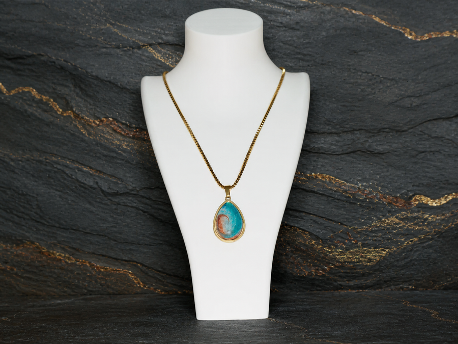 Tidal Rift 18K gold-plated teardrop pendant on a charcoal geological slate background