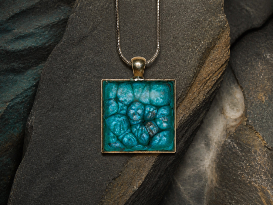 Silver square pendant with teal enamel-painted, resin-coated surface on dark slate and mineral textures