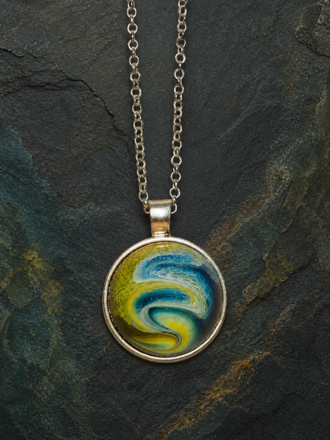 Front view of the blue green Verdant Gyre alcohol-ink resin pendant on dark slate