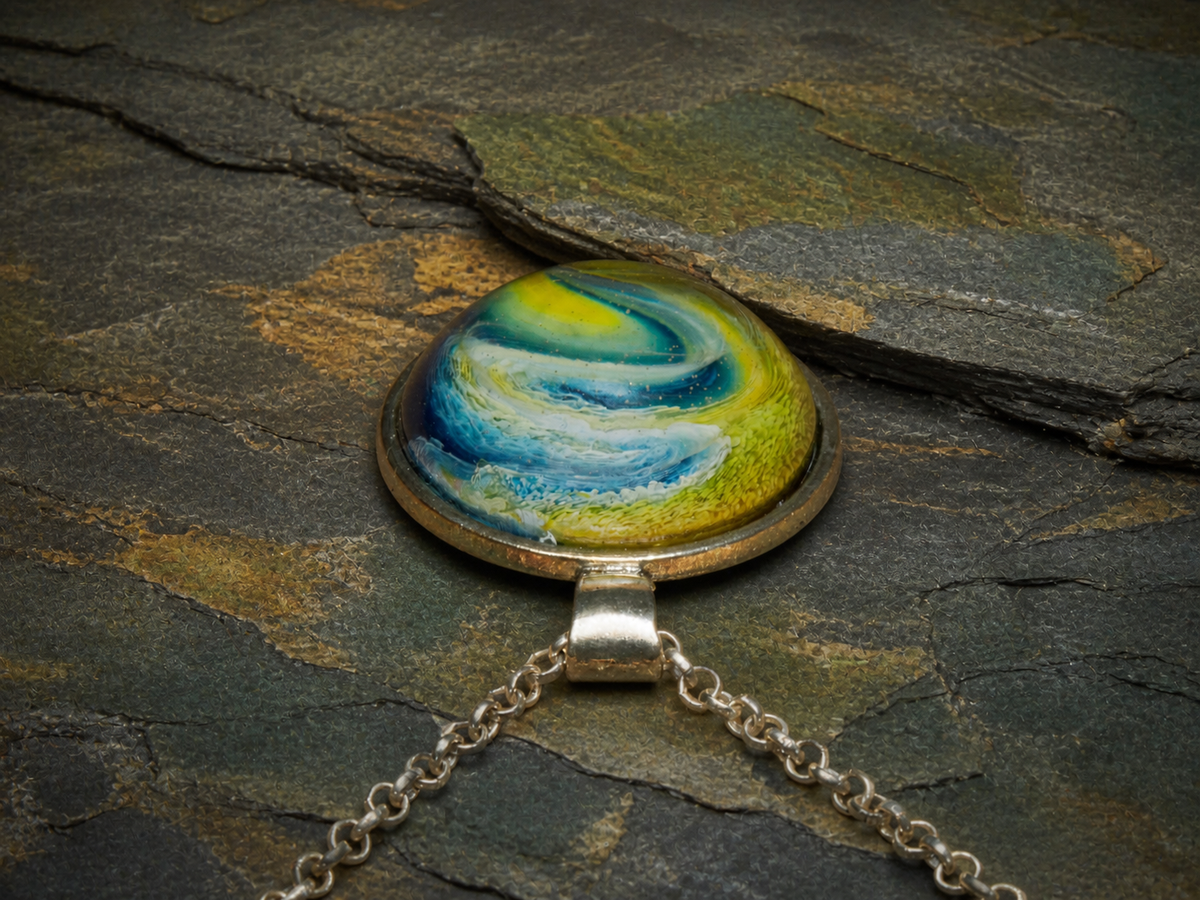 Low-profile view of the Verdant Gyre domed resin pendant and silver chain on layered slate