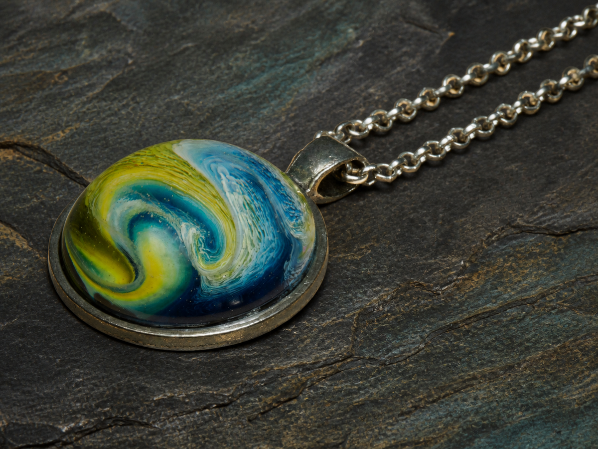 Angled close-up of the Verdant Gyre round silver-plated alcohol-ink pendant