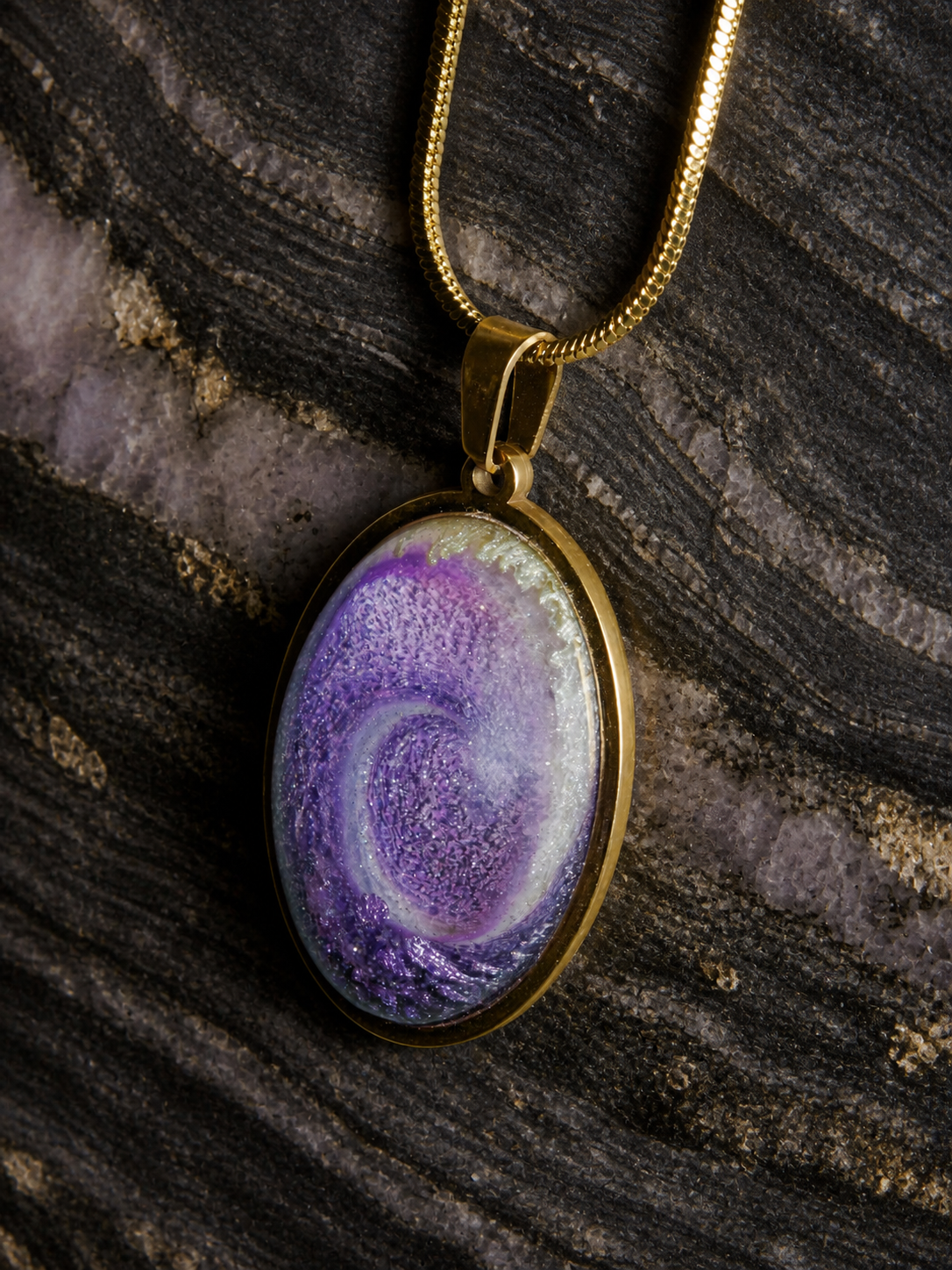 Violet Gyre oval resin pendant on charcoal rock, close front view